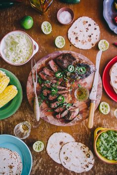 a wooden table topped with plates and bowls filled with different types of food next to corn on the cob