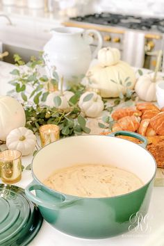 a green pot filled with soup sitting on top of a counter next to pumpkins