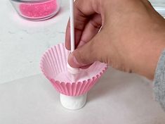 a hand holding a toothbrush over a pink cupcake wrapper on a table