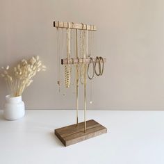 a wooden stand with several pairs of earrings on it next to a vase filled with flowers