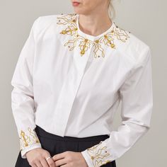 "Indulge in timeless glamour with our White Cotton Shirt adorned with Golden Embroidery Details. This elegant festive blouse is a statement piece crafted to elevate your ensemble effortlessly. Designed with meticulous attention to detail, it features hidden button placket and subtly padded shoulders, offering a refined silhouette that exudes sophistication. KEY FEATURES: - Luxurious white cotton fabric - Intricate golden embroidery details for a touch of opulence - Hidden buttons placket for a sleek finish - Subtly padded shoulders for added structure and elegance - Suitable for women size S - M - Excellent vintage condition - Dry clean only Fabric Information: 100% cotton MEASUREMENTS (while lying flat): Armpit to armpit: 52 cm | 20.5\" Length: 67 cm | 26.4\" Sleeves: 57 cm | 22.4\" Shoul Elegant Long Sleeve Embroidered Top With Floral Embroidery, Elegant Fitted Embroidered Shirt, Classic Floral Embroidered Tops For Work, Formal Festive Tops With Floral Embroidery, Festive Formal Tops With Floral Embroidery, Formal Festive Top With Floral Embroidery, Elegant Workwear Shirt With Embellished Collar, Elegant Embellished Spring Shirt, Formal Floral Embroidered Tops For Festive Occasions