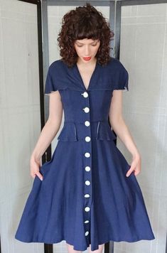 Vintage 40s Navy Blue Summer Dress White Buttons Shawl Collar Sweet summer frock that has a shawl collar, fitted bodice and nipped waist, and a wide cut circle skirt ending at id calf. There are large white buttons down the center for closure and the cutest little side panels, peplum style at the waist. Rear has a decorative sash at the waist, offset by two more buttons. Unlined. No tags. Label: none Size: no tag / fits like a medium / see exact measurements below to ensure fit Fabric: no tag / looks and feels like a sturdy but soft cotton of medium weight. Condition: very good with no visible issues Shoulders 15" Chest 38" Waist 26" Hips 58" Length 44" Fitted Navy Dress With Buttons, Fitted A-line Vintage Dress With Buttons, 1950s Style Fitted Dress With Buttons, Navy Fitted Vintage Dress, Navy Vintage Short Sleeve Dress, Navy Vintage Dresses With Buttons, Navy Vintage Dress With Buttons, Vintage Summer Dresses With Covered Buttons, Fitted 1950s V-neck Dress