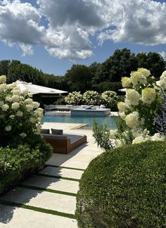 an outdoor patio with white hydrangeas and bushes around it, next to a swimming pool