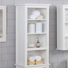 a white bathroom shelf with towels and other items on the shelves in front of it