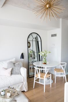 a living room with a white couch, table and mirror on the wall next to it