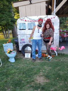 two people standing in front of a trailer with flamingos on the grass and decorations around it