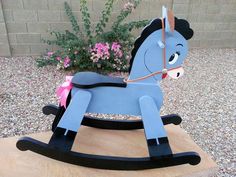 a wooden rocking horse with a pink ribbon on it's neck sitting in front of some flowers