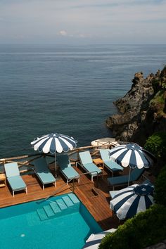 an outdoor pool with umbrellas and chairs next to the ocean