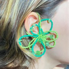 a close up of a person's ear wearing green beaded earrings with flowers on them