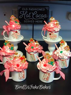 cupcakes are decorated with pink and gold ribbons on top of white mugs