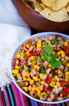 a white bowl filled with corn and salsa next to tortilla chips on a colorful table cloth