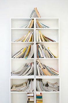 a book shelf filled with lots of books on top of each other in front of a white wall