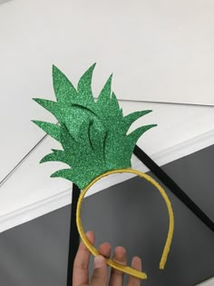 a hand holding a green paper pineapple headband with yellow tape around it's side