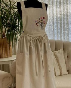 an apron dress is displayed on a mannequin in front of a couch and potted plant