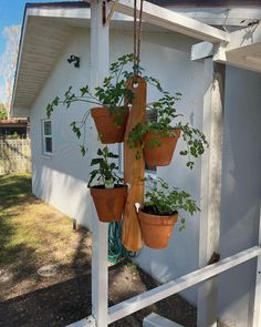 several potted plants are hanging from a wooden rack on the side of a house