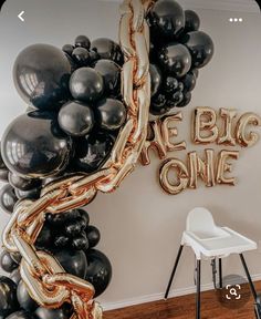 black and gold balloons with the words we're big one written on them are in front of a white chair