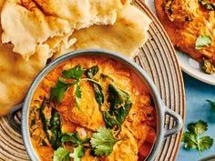 some food is in a blue bowl on a table with bread and other foods around it