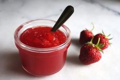 two strawberries sit next to a jar of strawberry jam