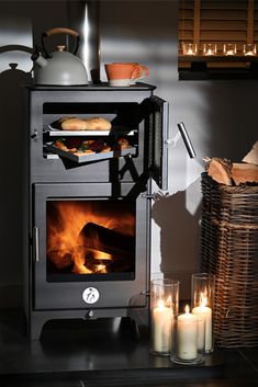 a wood burning stove in a kitchen next to some candles and baskets with food on them