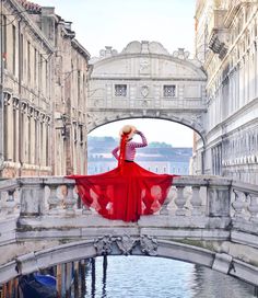 a woman in a red dress is standing on a bridge