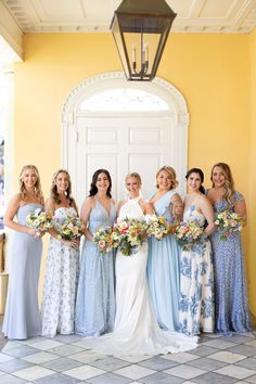 a group of women standing next to each other in front of a yellow wall holding bouquets