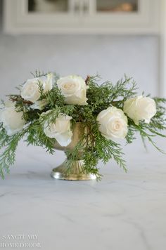 white roses and greenery in a gold vase on a marble countertop with cabinets