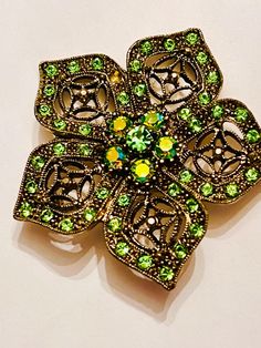 Vintage austria style  green and aurora borealis glass rhinestones set in a raised filagree  relief multi stone  detail flower setting. It is measuring  2 in diameter. Please be sure to view all of my photos. one tiny green stone missing otherwise no issues. Green Jeweled Brooch For Gift, Green Jeweled Brooches As Gift, Vintage Green Rhinestone Brooches, Green Vintage Rhinestone Brooches, Green Rhinestone Wedding Brooch, Green Rhinestone Wedding Brooches, Vintage Green Rhinestone Brooch, Ornate Green Brooches For Wedding, Flower Setting