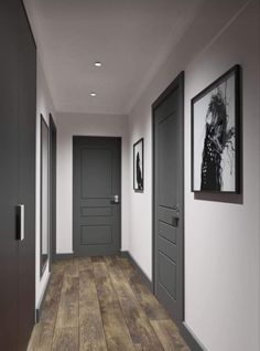 an empty hallway with two gray doors and pictures on the wall above it, along with hardwood flooring