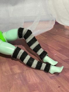 a green doll with black and white striped socks laying on top of a wooden floor