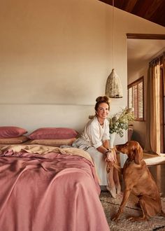 a woman sitting on a bed next to a brown dog and potted plant in front of her