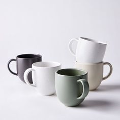 four coffee cups sitting side by side on a white surface, one black and one grey