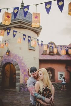 a man and woman hugging in front of a castle with lanterns hanging from the ceiling