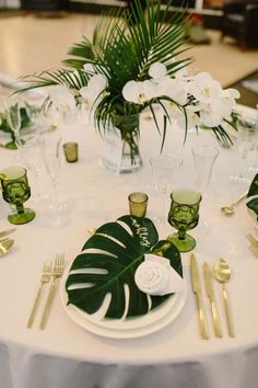 the table is set with green and white plates, silverware, and palm leaves