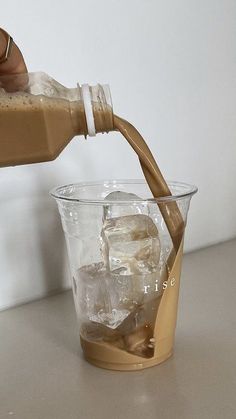 someone pouring some liquid into a glass with ice cubes