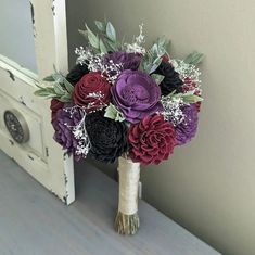 a bridal bouquet with purple and red flowers in front of a white door handle