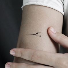 a woman's arm with a small bird tattoo on the left side of her arm