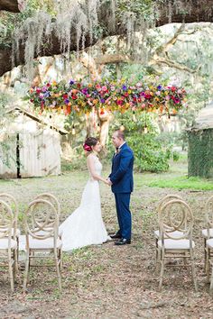 a bride and groom standing in front of an outdoor ceremony arch with flowers hanging from it