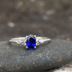 a blue sapphire and diamond ring sitting on top of a gray rock in front of some rocks