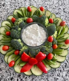 a platter filled with cucumbers, tomatoes, broccoli and dip