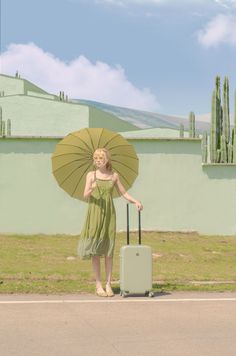 a woman in a green dress with an umbrella and suitcase