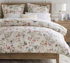 a bed with pink flowers on it in a bedroom next to a nightstand and lamp