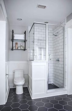 a white bathroom with hexagonal tile flooring and black tiles on the walls