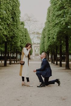 a man kneeling down next to a woman on the ground in front of some trees