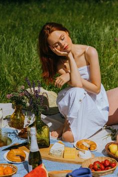 a woman is sitting on the grass with her picnic food and drinks in front of her