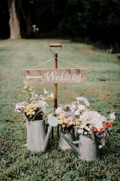 two metal watering cans with flowers in them and a sign that says wedding on it