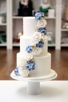 a three tiered cake with blue and white flowers on the top is sitting on a table