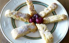 a white plate topped with pastries covered in powdered sugar and cherries on top of it