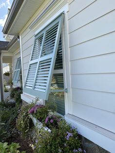 an open window on the side of a house with flowers growing in front of it