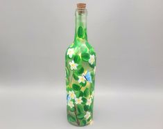 a green glass bottle with white flowers and leaves painted on the bottom is shown in front of a gray background