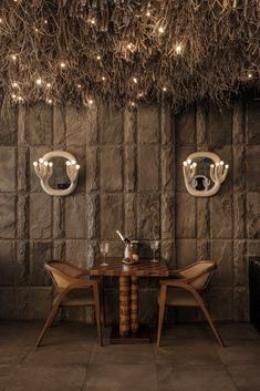 two chairs and a table in front of a stone wall with lights hanging from it